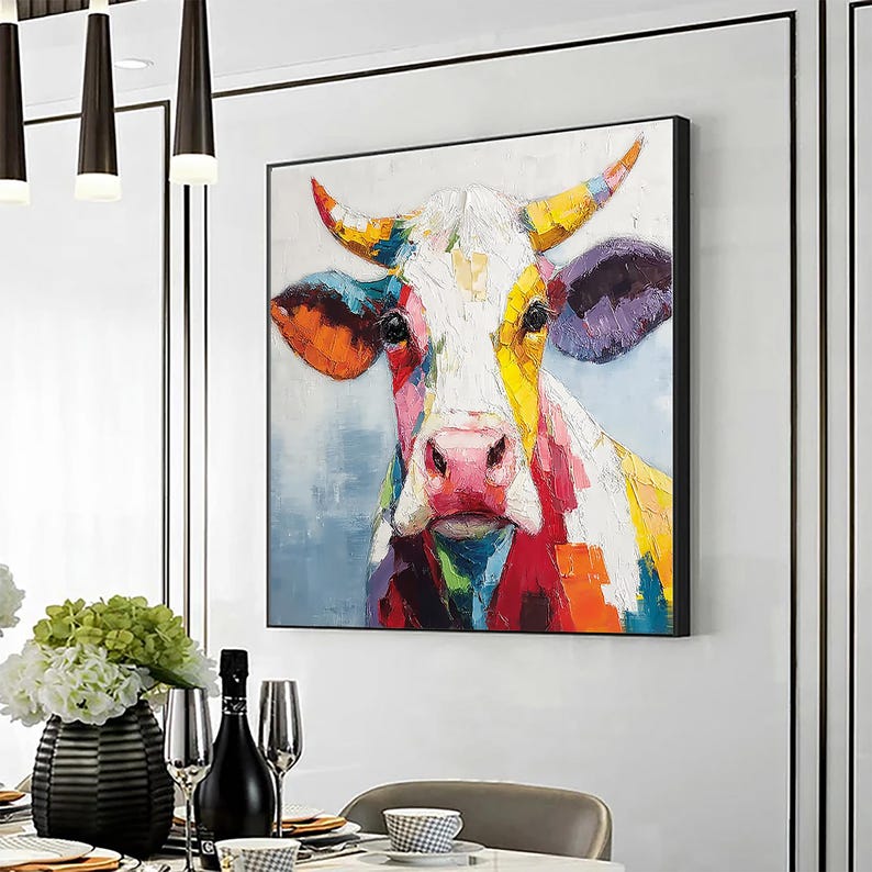 May include: A colorful cow portrait painting with a black frame. The cow's face is painted with vibrant brushstrokes of red, yellow, orange, purple, and blue. The background is a soft blue, creating a striking contrast.
