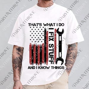 May include: White t-shirt with a graphic design featuring an American flag with a wrench and the text "THAT'S WHAT I DO, I FIX STUFF, AND I KNOW THINGS". The design is in black and red.