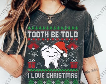 Może przedstawiać: Ciemnoszara koszulka z świątecznym motywem bożonarodzeniowym. Koszulka zawiera napis "TOOTH BE TOLD I LOVE CHRISTMAS" z uśmiechniętym zębem w czapce Świętego Mikołaja, płatkami śniegu i pudełkami z prezentami. Projekt jest w kolorach czerwonym, zielonym i białym.