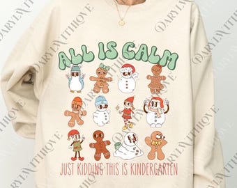 Könnte beinhalten: Beiges Sweatshirt mit einem skurrilen Design mit Cartoon-Lebkuchenmännchen, Schneemännern und einem Elf. Der Text "ALL IS CALM" in grünen Buchstaben steht über dem Satz "JUST KIDDING THIS IS KINDERGARTEN" in Rot.