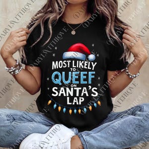 May include: Black t-shirt with the text "MOST LIKELY TO QUEEF ON SANTA'S LAP" in white and blue. A Santa hat graphic is above the text, and a string of Christmas lights is below. The shirt is a festive holiday design.