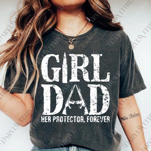 May include: Dark gray t-shirt with the words "GIRL DAD" in large, distressed white letters. The word "DAD" features a stylized image of two rifles. Below the text is the phrase "HER PROTECTOR, FOREVER".