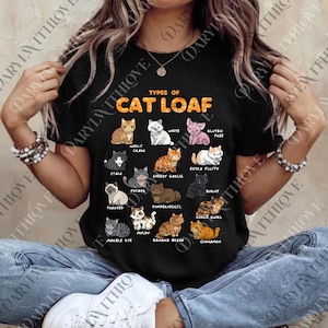 May include: Black t-shirt featuring the text "TYPES OF CAT LOAF" above illustrations of various cat breeds. The shirt includes cat breeds such as "Whole Grain", "White", "Extra Fluffy", and "Cinnamon".