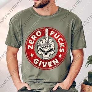 Puede incluir: Camiseta verde oliva con un gráfico circular rojo desgastado. El diseño presenta una calavera con el dedo medio levantado y el texto "ZERO FUCKS GIVEN". La camiseta tiene cuello redondo y mangas cortas.