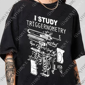 Op de afbeelding: Zwart T-shirt met de witte tekst "I STUDY TRIGGERNOMETRY". Het shirt heeft een gedetailleerd diagram van een handvuurwapen, met verschillende onderdelen gelabeld. Het ontwerp is een technische illustratie.
