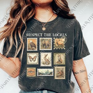 A woman wearing a black t-shirt with a graphic design of postage stamps featuring various animals, including a bear, eagle, and deer.