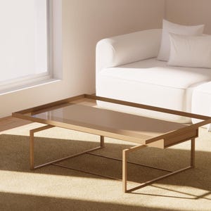 May include: A rectangular coffee table with a glass top and a light brown wooden frame. The table is set on a beige carpet in front of a white sofa and a window with white curtains. The table's dimensions are approximately 48 inches long and 24 inches wide.