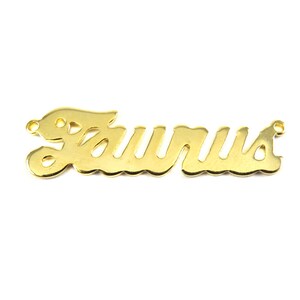 May include: Gold-colored metal charm with the word "Taurus" written in a cursive font.