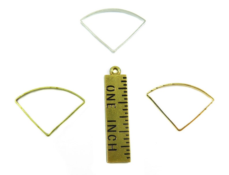 May include: An assortment of metal fan-shaped jewelry findings in silver, gold, and brass tones. A brass ruler with the text "ONE INCH" is also present, indicating the size of the findings. These components are ideal for crafting earrings, pendants, or other jewelry.
