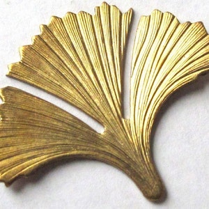 May include: A detailed, golden-colored metal ginkgo leaf. The leaf has a fan-like shape with intricate veining and a textured surface. The edges are gently scalloped, and the overall design is elegant and natural.