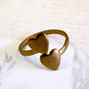 May include: A gold-toned ring with two heart-shaped designs. The hearts are connected and face opposite directions.