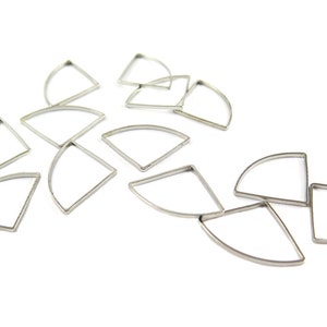 May include: A collection of silver-colored, fan-shaped metal frames scattered on a white surface. Each frame has a curved top and two straight sides, creating a geometric design. The frames are likely for jewelry making or crafting.