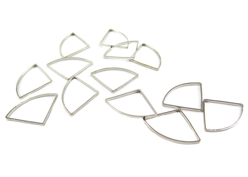 May include: A collection of silver-colored, fan-shaped metal frames scattered on a white surface. Each frame has a curved top and two straight sides, creating a geometric design. The frames are likely for jewelry making or crafting.