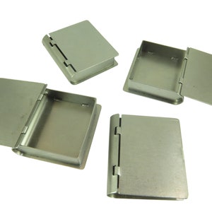 May include: Four silver metal book-shaped boxes with hinged lids. The boxes are closed and open, showing the interior.