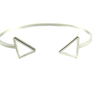 May include: A silver-colored open cuff bracelet with two triangular accents. The bracelet has a simple, modern design, with the triangles at each end of the open cuff. The bracelet is shown against a white background.
