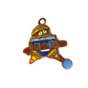 May include: A copper charm with a cartoon robot design. The robot is wearing a blue and yellow suit and has a red and yellow hat. The robot is holding a blue ball.