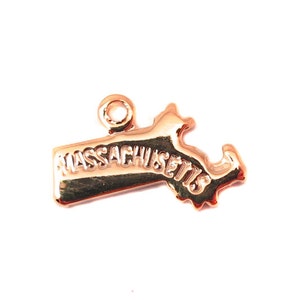 Może przedstawiać: Złoty metalowy charm w kształcie stanu Massachusetts z wytłoczonym napisem "MASSACHUSETTS".