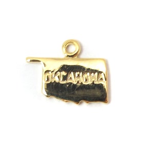May include: Gold-colored metal charm shaped like the state of Oklahoma with the word "OKLAHOMA" engraved on it.