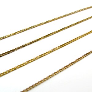 May include: Three strands of gold chain, each with a different length, are laid out on a white surface.