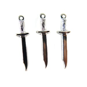 May include: Three silver-colored dagger charms with a textured handle and a small loop at the top for attaching to jewelry. The blades have a curved edge. The charms are displayed against a white background.