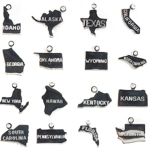 May include: A set of 16 silver charm pendants shaped like the outlines of different US states. Each pendant has the state name engraved on it.
