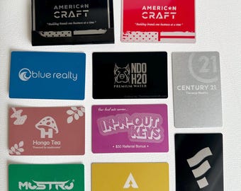 May include: A collection of business cards featuring various logos and slogans. The cards are made of metal and have a polished finish. Some of the logos include a mushroom, a house key, and a water bottle. The slogans include "Building brands one business at a time", "Your local ute expert", and "Your private oasis awaits".