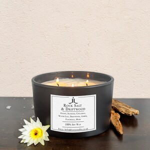 May include: A black candle jar with a white label that reads "Rock Salt & Driftwood". The label lists the fragrance notes: ozone, seaweed, cyclamen, water lily, driftwood, amber, patchouli, and musk. The candle is made with 100% soy wax. The email address hello@leoracandles.co.uk is printed on the label.