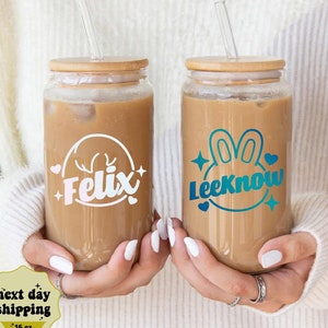 May include: Two 16 ounce glass tumblers with bamboo lids and clear straws. The tumblers are filled with iced coffee. One tumbler has a white decal with the name "Felix" and a deer head design. The other tumbler has a blue and green decal with the name "LeeKnow" and a bunny rabbit design.