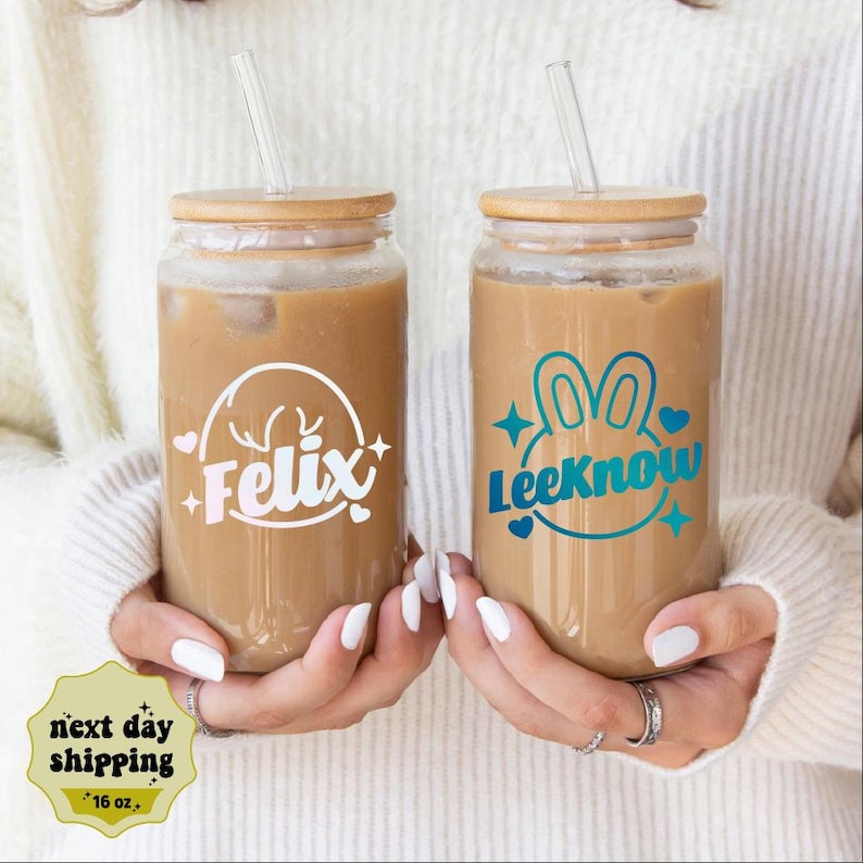 May include: Two 16 ounce glass tumblers with bamboo lids and clear straws. The tumblers are filled with iced coffee. One tumbler has a white decal with the name "Felix" and a deer head design. The other tumbler has a blue and green decal with the name "LeeKnow" and a bunny rabbit design.