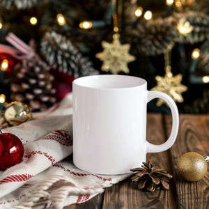 May include: A white ceramic mug with a handle, sitting on a wooden surface with a festive background of pine branches and Christmas lights.
