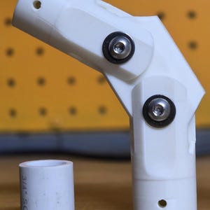 May include: A white, 3D-printed adjustable elbow joint with two metal screws and a small white pipe section. The elbow has a pivoting design and is likely used for plumbing or construction. The pipe section has the text "3/4" SCH4".