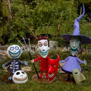 Pode incluir: Três figuras de personagens de O Estranho Mundo de Jack. As figuras incluem um esqueleto, um diabo e uma bruxa. A figura do esqueleto tem uma cabeça de caveira e uma roupa preta. A figura do diabo é vermelha e segura uma máscara vermelha. A bruxa é roxa.