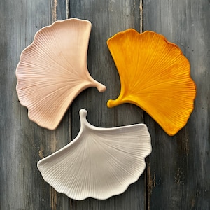 Può includere: Tre piatti in ceramica a forma di foglie stilizzate. I piatti sono in tonalità rosa, beige e giallo.