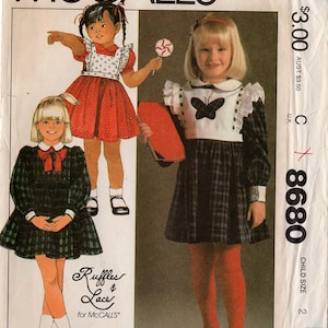 May include: McCall's sewing pattern for children's dresses. The pattern features illustrations of girls in various dresses, including a red dress with white accents, a plaid dress, and a dress with a butterfly design. The price is $3.00.