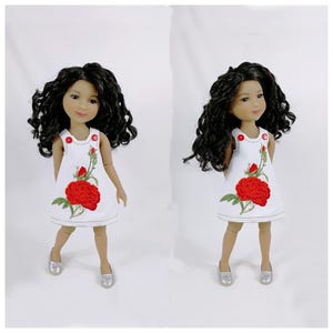 Può includere: Due bambole con capelli ricci scuri e pelle chiara. Indossano abiti bianchi con ricami di rose rosse e scarpe argentate. Gli abiti hanno dettagli con bottoni rossi. Le bambole sono su sfondo bianco.