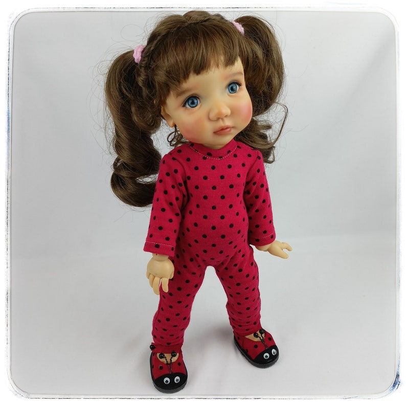 May include: A red and black polka dot jumpsuit with long sleeves and a round neckline. The doll is wearing red shoes with black ladybug eyes.