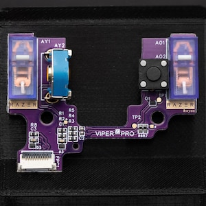 Może przedstawiać: Zbliżenie fioletowej płytki drukowanej Razer Viper Pro. Płytka zawiera różne komponenty, w tym przyciski, przełączniki i złącza. Widoczne jest logo Razer oraz napis "VIPER PRO".