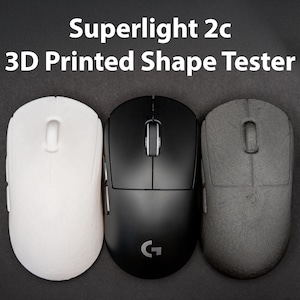 Può includere: Tre mouse per computer bianchi, neri e grigi, disposti su una superficie scura. Il testo "Superlight 2c 3D Printed Shape Tester" è in alto. Il mouse nero ha un logo "G".