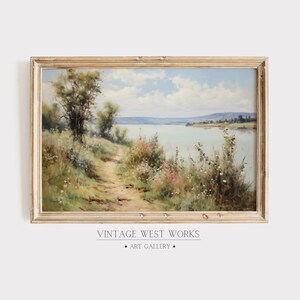 May include: A vintage landscape painting depicting a path leading to a lake with a forest in the background. The painting is framed in a light wood frame.