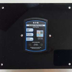 May include: A black surge protector with a blue and white label that reads "F.T.N. Surge Protector CHSPT2ULTRA". The label also includes the text "Type 2 SPD", "AC Power Protection", "Indoor/Outdoor Use", "Surge Current Capacity 108A", and "STATUS INDICATORS".