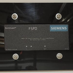 May include: A black metal plate with a silver Siemens FSPD BoltShield label. The label has the text "FSPD" and "Siemens" in white lettering. The label also has the text "BoltShield" in white lettering with a trademark symbol. The label has the text "GUSTL, ON - Protection Operating, OFF - Loss of Power Protection,  W22 - Relaying & Alarm Condition" in small white lettering.