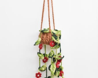 May include: A crocheted hanging planter with green leaves and red flowers. The planter is brown and has a rope hanger.