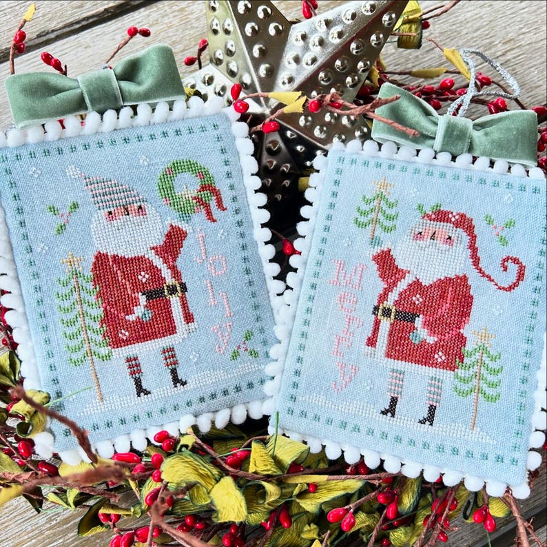May include: Two blue and white cross-stitch ornaments featuring Santa Claus with the words "Jolly" and "Merry" on each ornament.