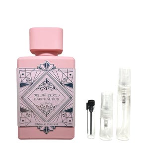 May include: A pink perfume bottle with a matching cap, featuring a decorative label with Arabic script and the words "NOBLE BLUSH." Accompanied by three small sample vials and a spray applicator.