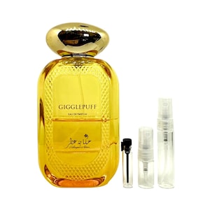 May include: A gold bottle of Gigglepuff Eau de Parfum with a gold cap and a textured design. The bottle is sitting on a white background with three small clear glass bottles with spray tops.