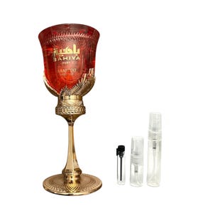 May include: A ruby red perfume bottle with gold accents and the text "BAHIYA RUBY ARABYAT PRESTIGE". The bottle is tall and ornate, with a decorative base and a matching stem. Several small sample bottles are next to the perfume bottle.