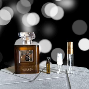 May include: A brown glass bottle of perfume with a silver cap. The bottle has a label that says "Charuto Tobacco Vanille Pandora Scents". There are three small glass bottles with caps.