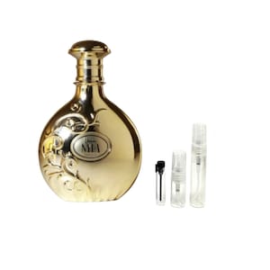 May include: A gold-colored perfume bottle with a decorative floral design and the word "NYLA" on a label. Several small, clear sample vials are next to the bottle, suggesting a fragrance product.