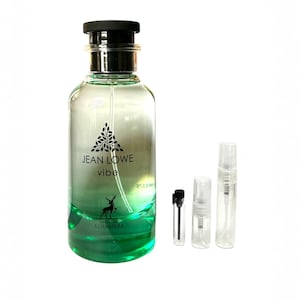 May include: A clear glass perfume bottle with a black cap and silver accents. The bottle has a gradient of green and clear liquid inside, with the text "JEAN LOWE vibe" and a deer logo. Several small sample vials are next to the bottle.