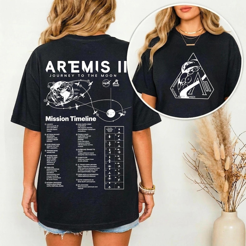 May include: Black t-shirt with white text and graphics. The back of the shirt features the words "Artemis II Journey to the Moon" above a mission timeline graphic. The front of the shirt has a white geometric design with the text "NASA".